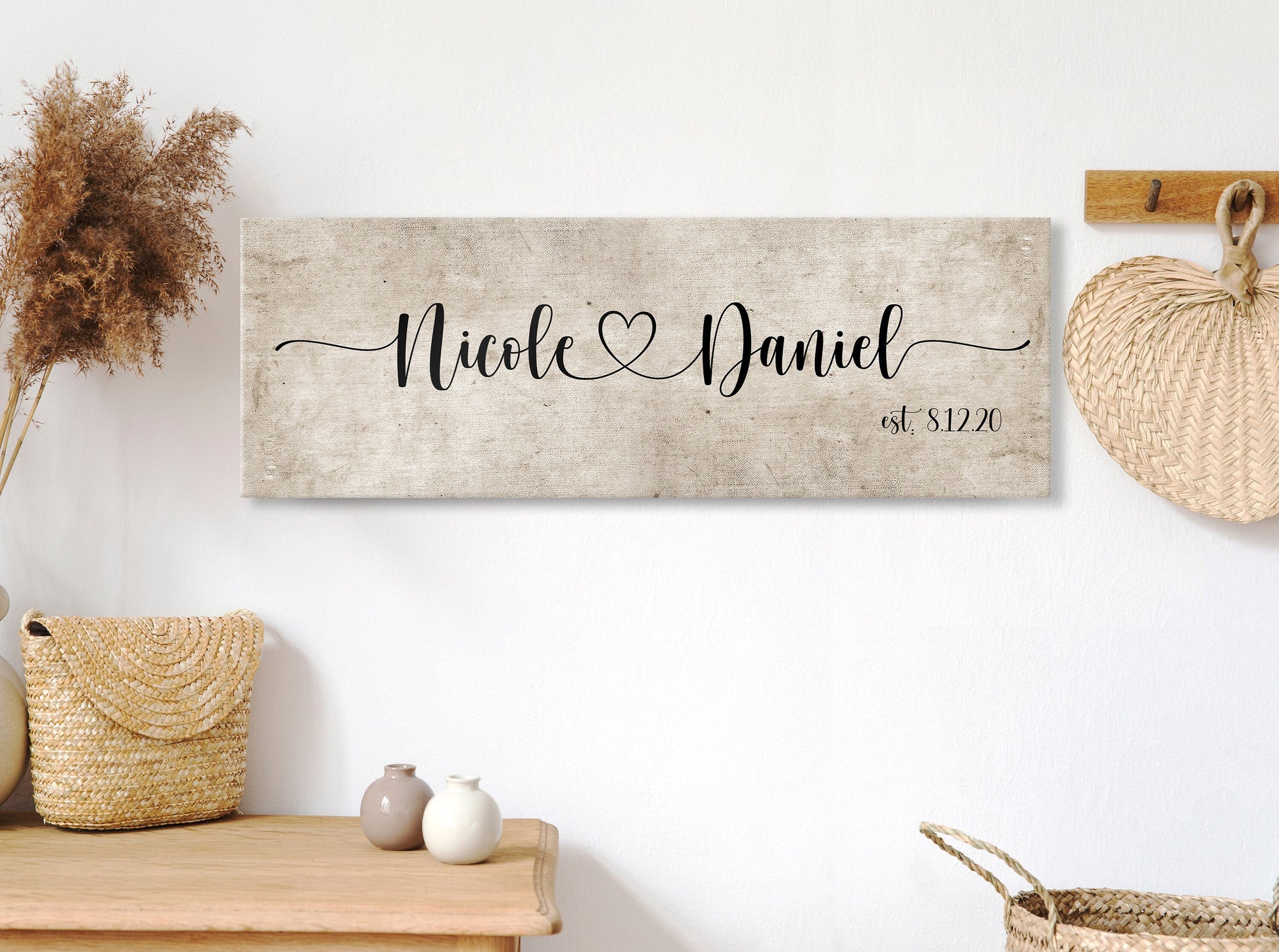 rustic cotton canvas name sign, with 2 first names connected by a heart in a whimsical and playful typeface. A personalized name sign on vintage cotton hangs on wall above bench in entry of home.