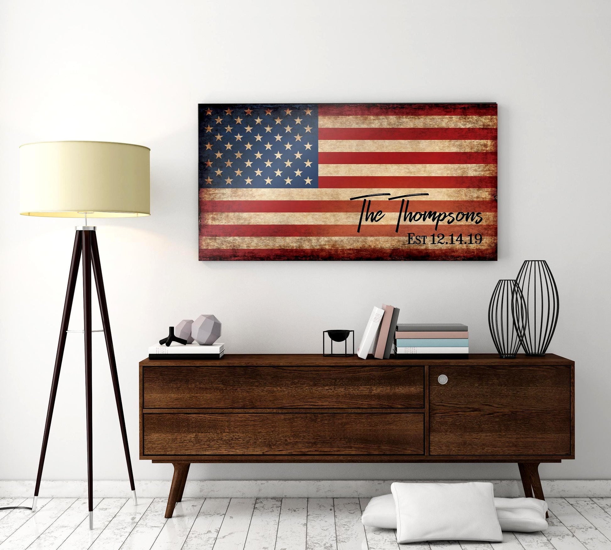 A distressed wood sign with an American flag design and the text "The Thompsons Est 12.14.19". The sign is hanging on a white wall above a wooden dresser.