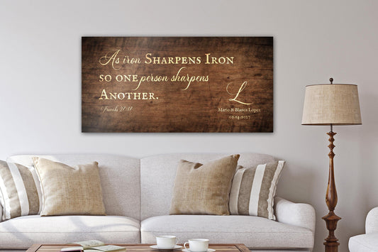 A handcrafted and personalized rustic wooden sign hangs above a linen sofa in "Stained Birch" finish - one of four finish options. The bible verse, "As iron sharpens iron; so one person sharpens another" as well as the names and established date of the recipients' are included on this handcrafted rustic wall decor.

Courtesy of Honeycomb Proverbs