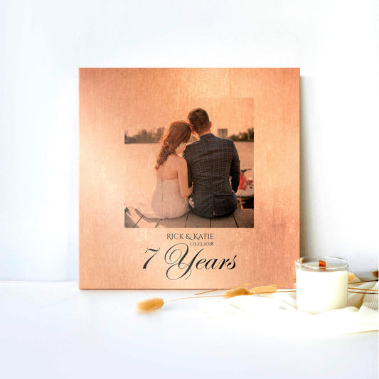 Copper 7 Year Anniversary Photo Plaque is shown leaned against a white backdrop with a candle and silk cloth on the lower right of the frame. The copper plaque centers the photograph center in a square shape with the names of the couple in the photo beneath, and "7 Years" in a large calligraphy at the bottom. The plaque is distressed with rustic, vintage style with the photo blending with hues of the copper.

Courtesy of Honeycomb Proverbs