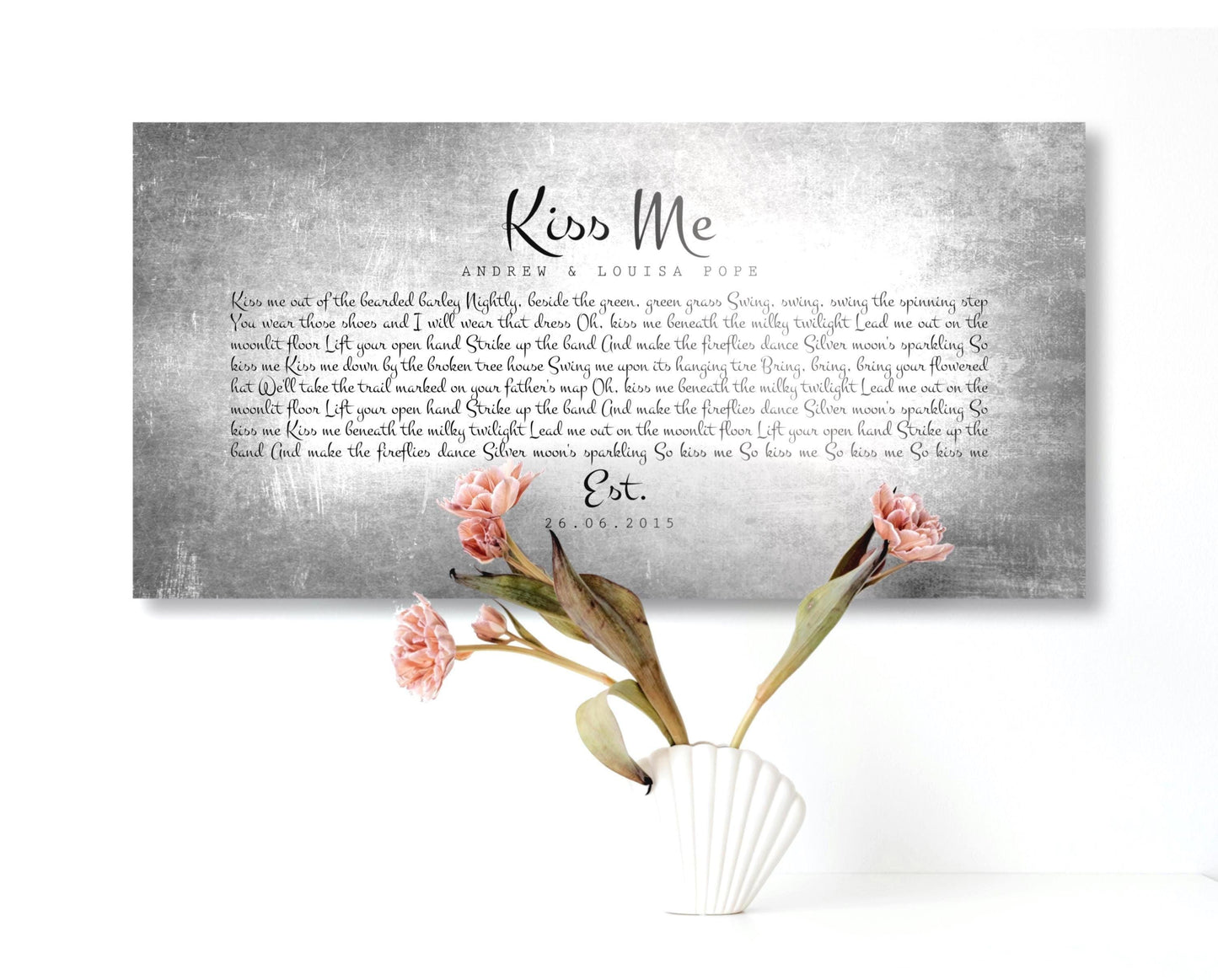 A tarnished metal song lyric sign hangs on a white wall with a white shell vase on a table beneath it with pink flowers.

Tin Anniversary Gift Lyrics Art courtesy of Honeycomb Proverbs